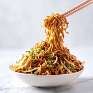 A dynamic, photorealistic shot of savory chow mein being lifted by chopsticks from a shallow bowl, highlighting the glistening texture of the noodles and sauce. (Chow Mein Recipe)