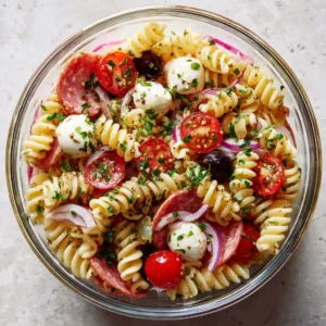 Top-down view of a High-Protein Italian Pasta Salad showing glossy rotini, halved tomatoes, and herb vinaigrette.