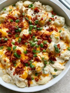 Close-up high-angle shot of creamy Crack Chicken Gnocchi with glossy sauce and crispy bacon in a white skillet.