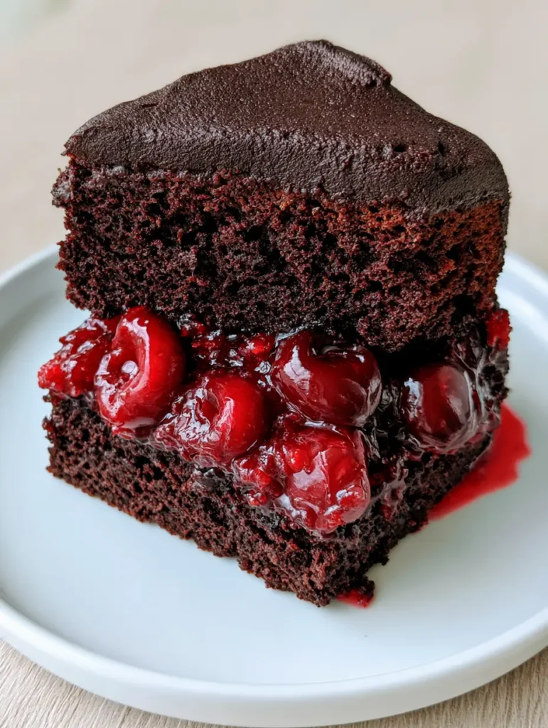 Handheld smartphone photo of a thick slice of Chocolate Cake with Cherry Pie Filling with glossy syrup oozing on a white ceramic plate.