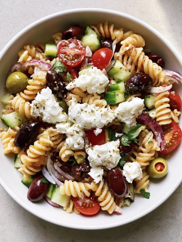 Greek Olive Pasta Salad with whole Kalamata olives, stuffed green olives, and large crumbles of feta cheese on a grey stone background.