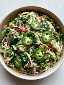 High-angle view of Jalapeño Slaw in a ceramic bowl featuring green and purple cabbage ribbons and sliced jalapeños with seeds.