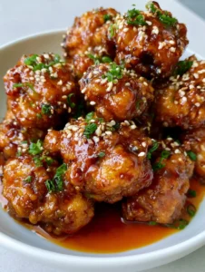 Close-up of golden-brown fried chicken pieces in a thick translucent orange sauce with sesame seeds. (Orange Chicken Recipe)