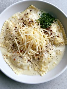 Close-up of al-dente cheese ravioli draped in an opaque white Garlic Parmesan Ravioli Sauce with specks of black pepper and minced garlic.