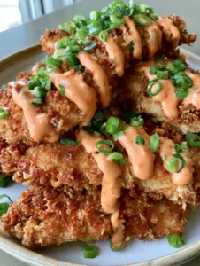 A handheld smartphone photo of golden crispy panko-crusted Bang Bang Chicken tenderloins with orange chili-mayo sauce.