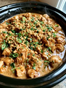 Close up of moist chicken chunks coated in thick creamy peanut sauce with visible steam and garnishes. (Slow Cooker Peanut Chicken)
