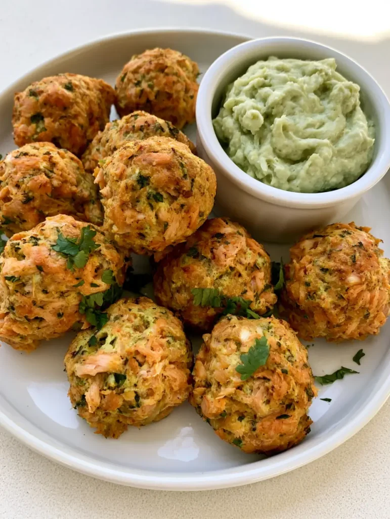 Close up of Salmon Meatballs on a white plate with a ramekin of pale-green avocado sauce.