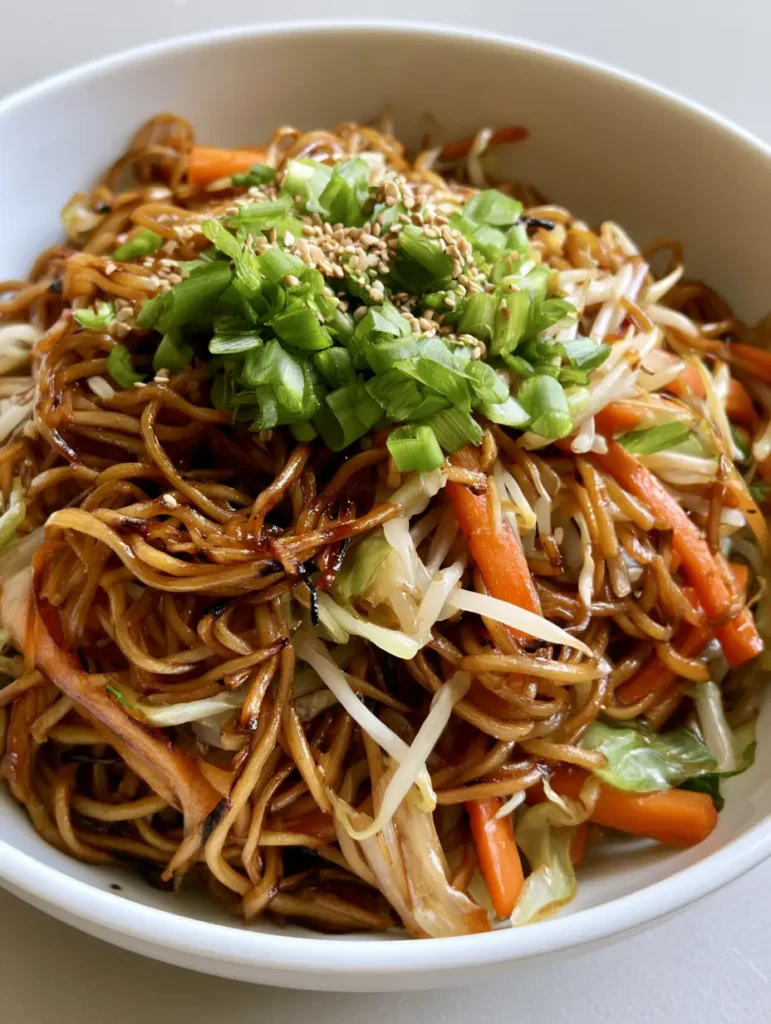 Close up of stir-fried wheat noodles with a dark savory soy glaze and green scallions. (Easy Chow Mein Recipe)