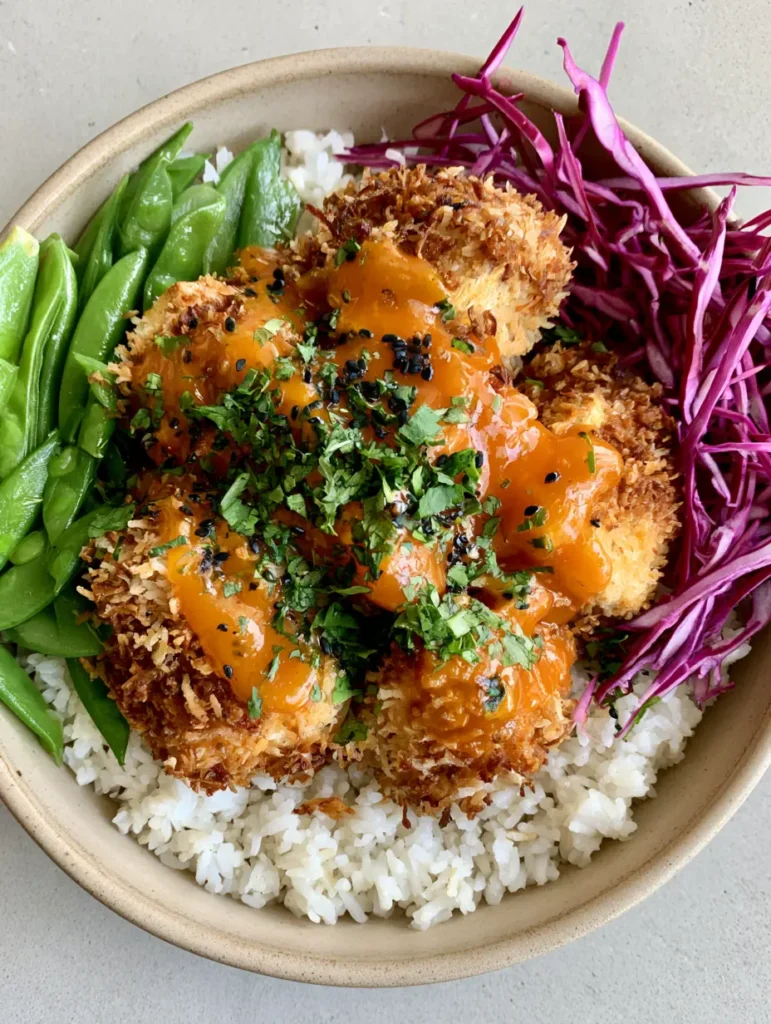 Overhead view of a ceramic bowl filled with coconut crusted tofu cubes, steamed jasmine rice, and fresh vegetables. (Coconut Crusted Tofu Bowl)