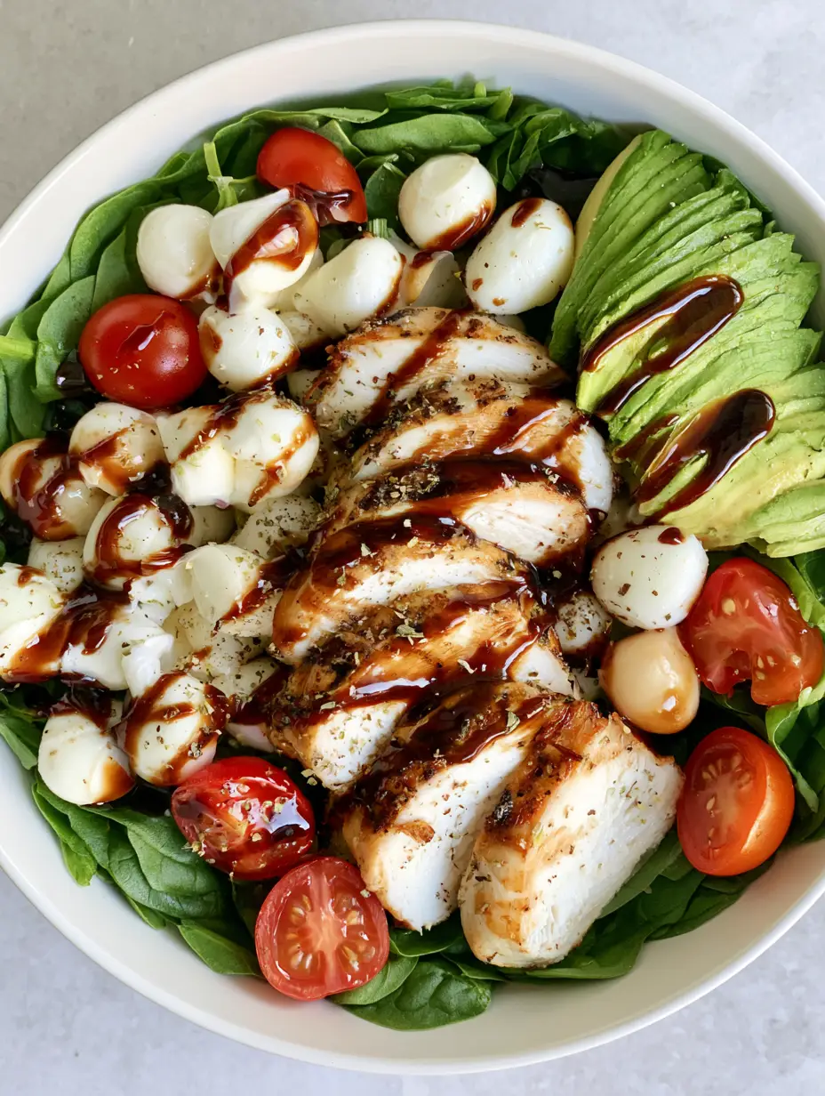 Top-down view of Baked Chicken Salad in a white bowl with spinach, avocado, and balsamic vinaigrette.