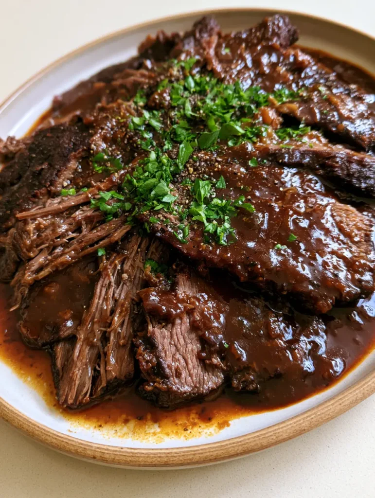 Handheld photo of Slow Cooker Beef Brisket slices on a white ceramic platter.