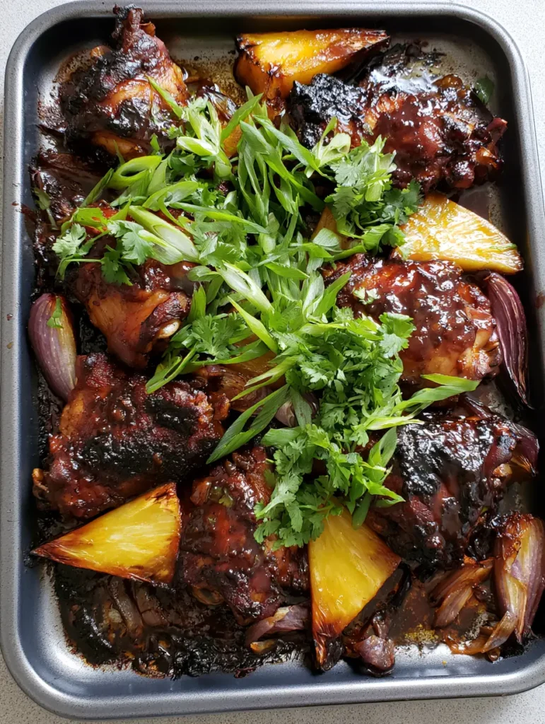 Overhead view of a metallic baking sheet featuring Jamaican Pineapple Jerk Chicken, caramelized pineapple wedges, and green scallions.