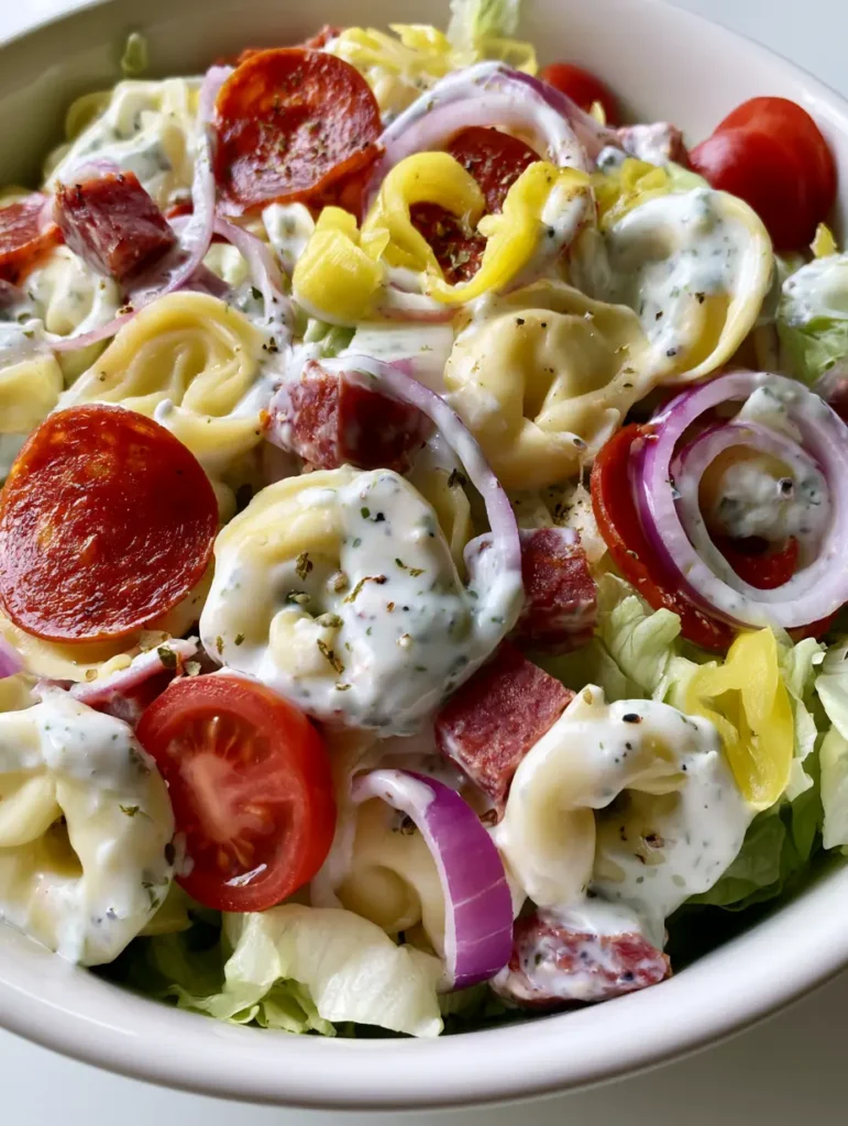 Close-up handheld photo of Italian Grinder Tortellini Salad with creamy dressing and shredded lettuce. (Italian Grinder Tortellini Salad)