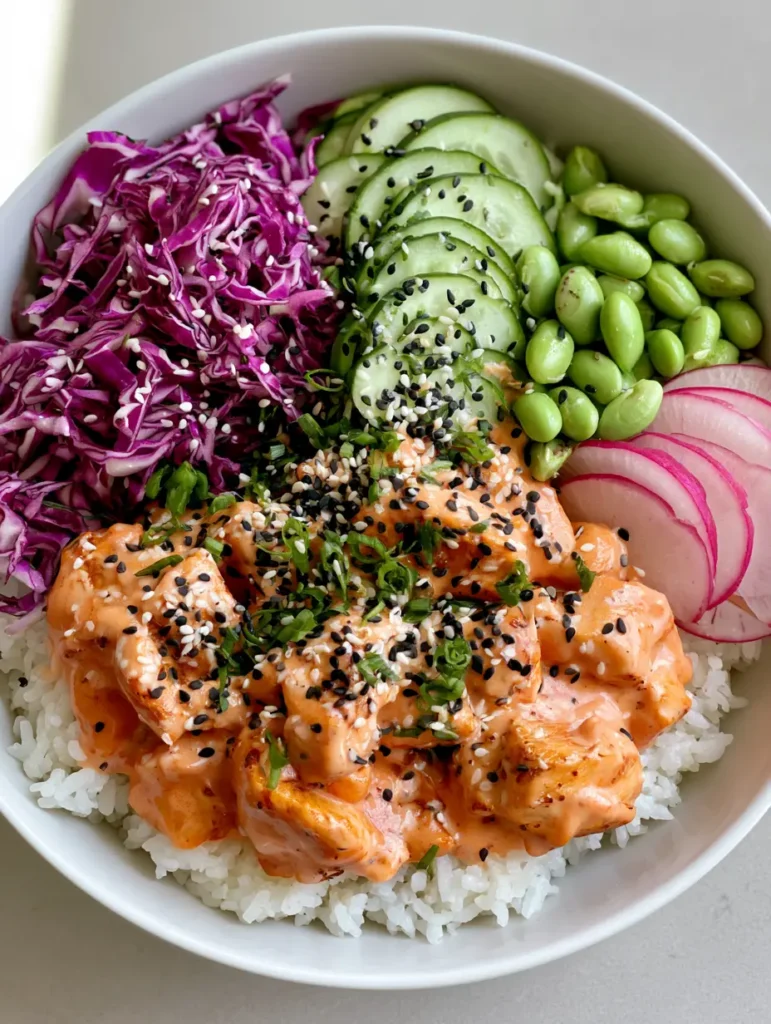 Bang Bang Chicken Bowl: The Ultimate 30-Minute Meal Prep 1 Close up of seared chicken chunks coated in glossy orange-pink bang bang sauce inside a white ceramic bowl.