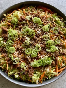 A close-up smartphone photo of ginger ground beef and cabbage stir fry in a dark skillet showing glossy sauce and charred edges. (Ginger Ground Beef and Cabbage Stir Fry)