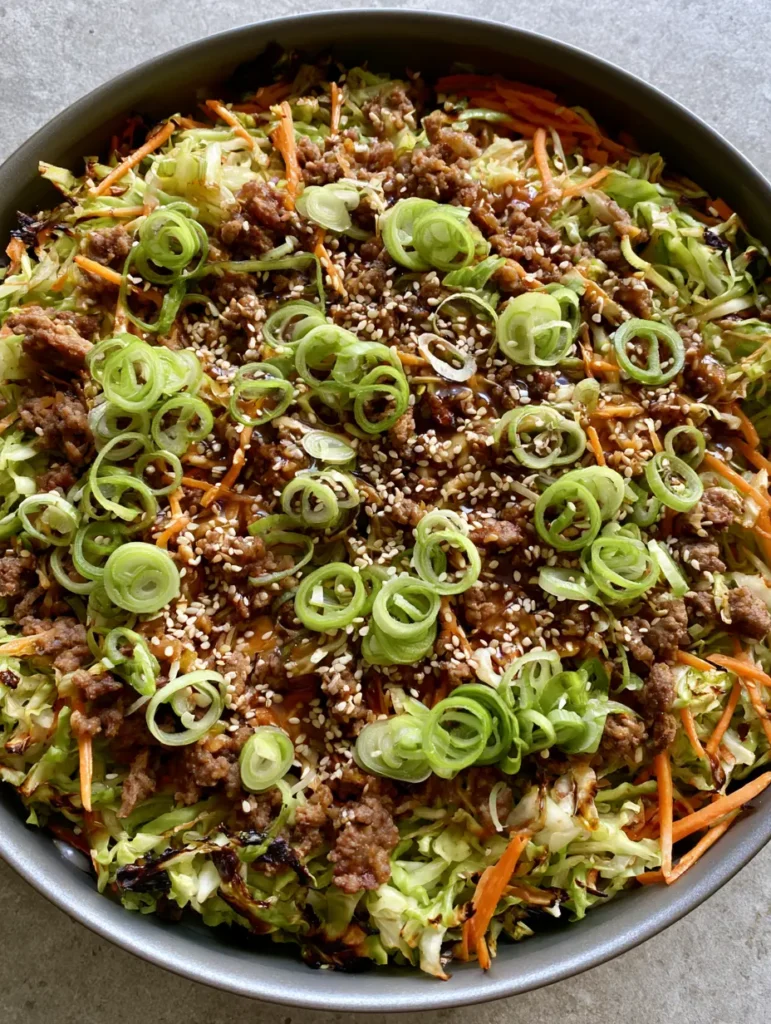 A close-up smartphone photo of ginger ground beef and cabbage stir fry in a dark skillet showing glossy sauce and charred edges. (Ginger Ground Beef and Cabbage Stir Fry)