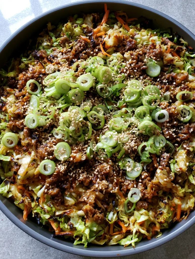 A top-down view of the completed Ginger Ground Beef and Cabbage Stir Fry garnished with scallions and sesame seeds on a stone countertop.