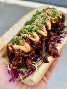 A loaded Korean Steak Sandwich featuring seared beef strips, colorful cabbage slaw, and green onions on a toasted baguette. (Korean Steak Sandwich)