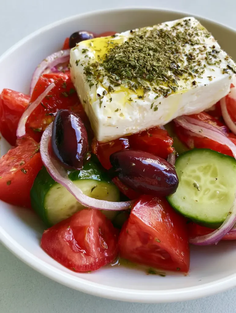 Visual details of Authentic Greek Salad components: thick cucumber half-moons and vibrant red tomato chunks lightly coated in oil.
