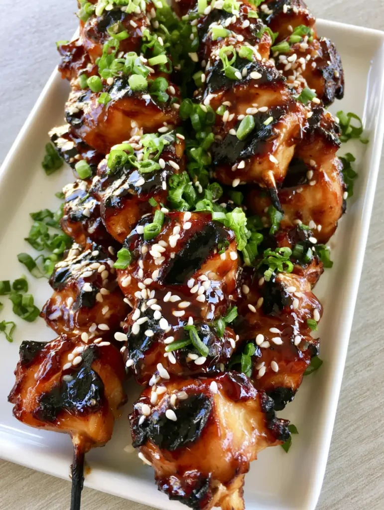 Honey Garlic Chicken Skewers: The Ultimate Sticky Grilled Dinner 1 Honey Garlic Chicken Skewers resting on a white ceramic plate with visible sesame seeds and chopped onions.