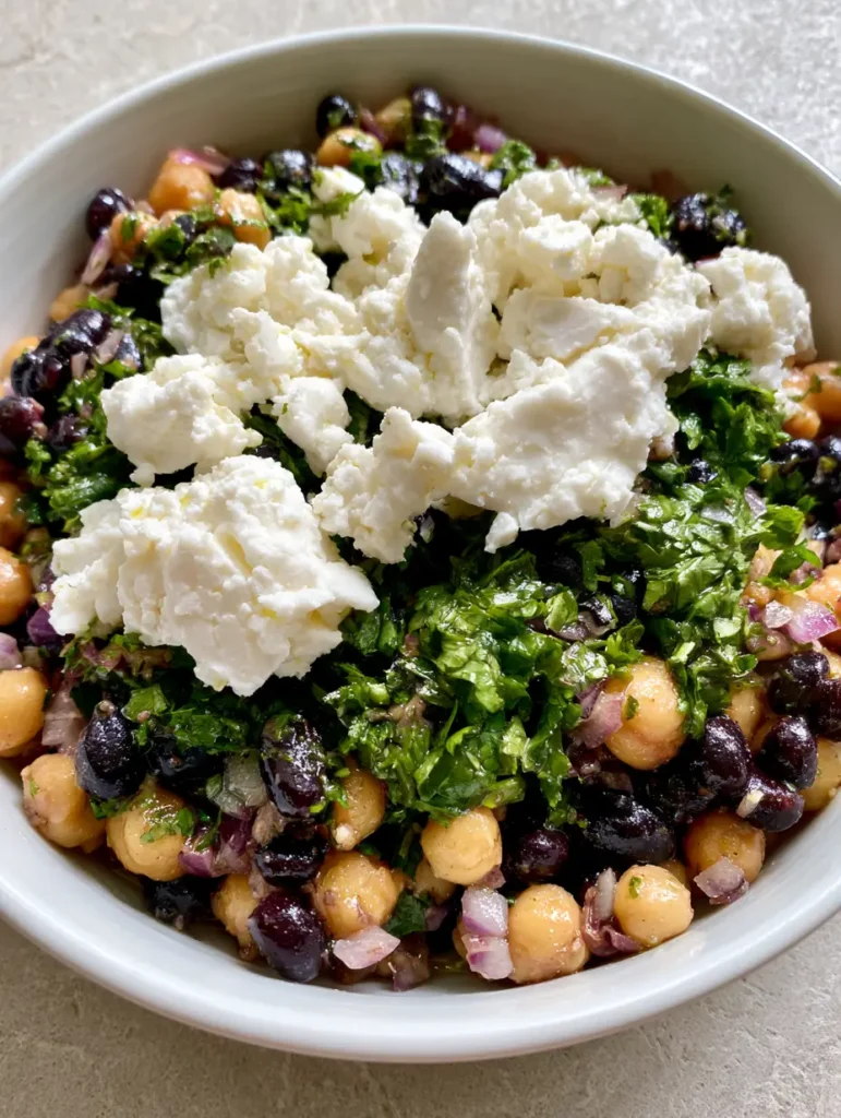 Chickpea and Black Bean Salad with Feta and Lime 1 Close up of matte white feta crumbles on a bed of tan chickpeas and glossy black beans.