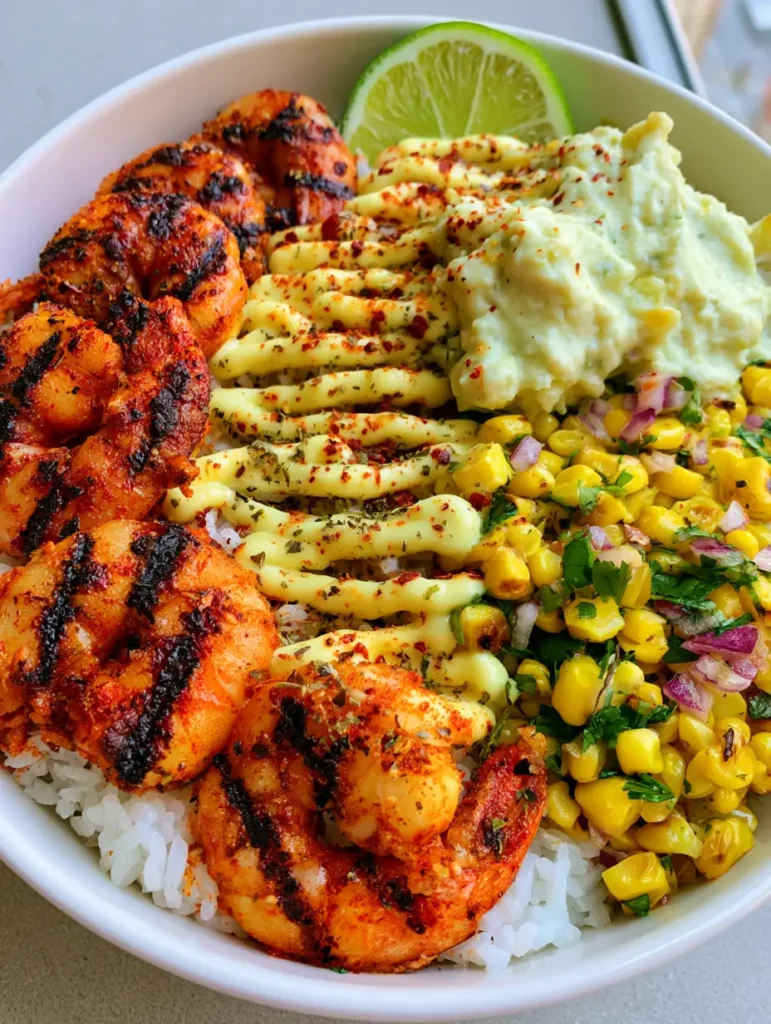 Top-down view of a white ceramic bowl containing succulent charred shrimp, fluffy rice, and pale green avocado mash for a Grilled Shrimp Bowl.
