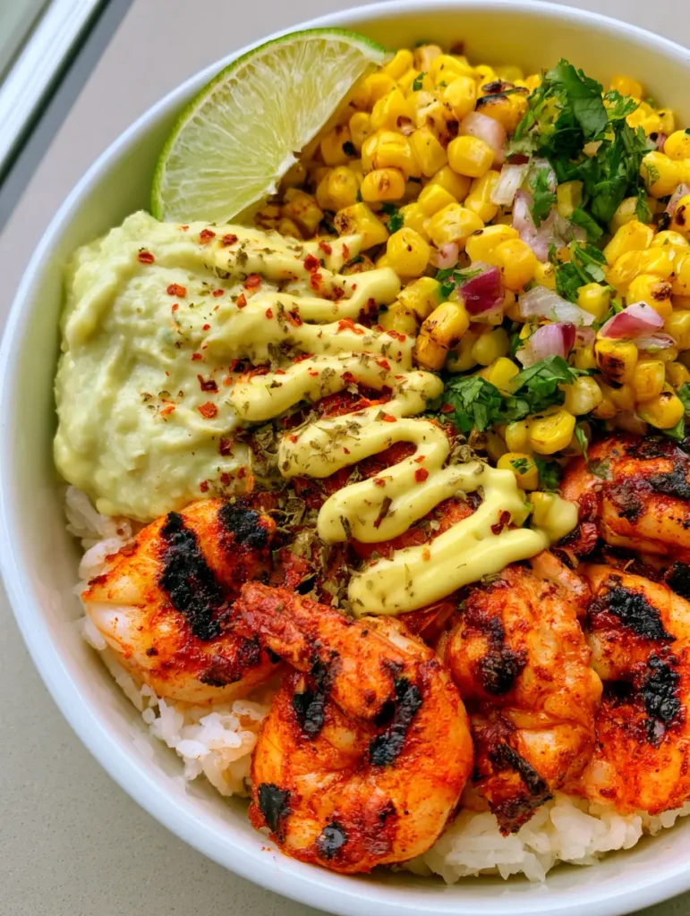 Detailed shot of the corn salsa and lime crema drizzle on a Grilled Shrimp Bowl with visible red chili flakes.