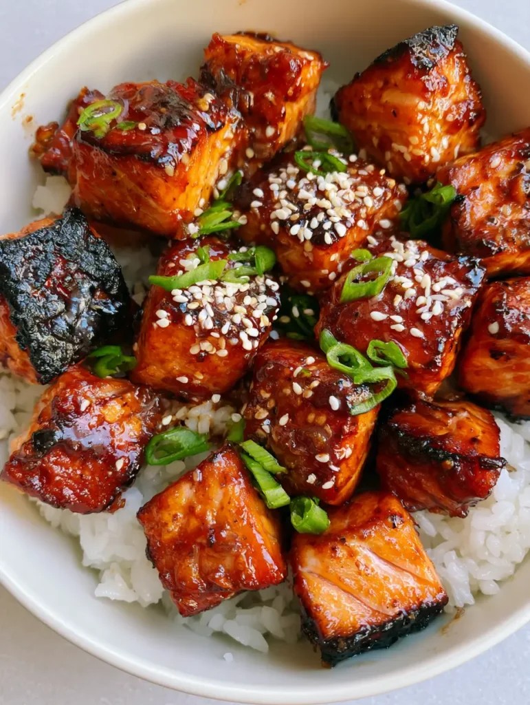 Top-down view of seared honey garlic salmon bites showing crispy edges and green onion garnish. (Honey Garlic Salmon Bites)