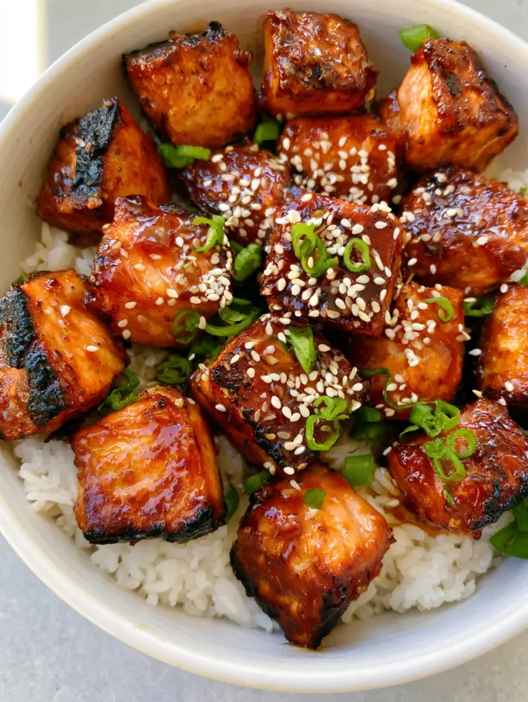 Honey Garlic Salmon Bites: The Ultimate 15-Minute Sticky Glazed Dinner 1 Detailed shot of glazed salmon bites with caramelized edges and white sesame seeds on jasmine rice.