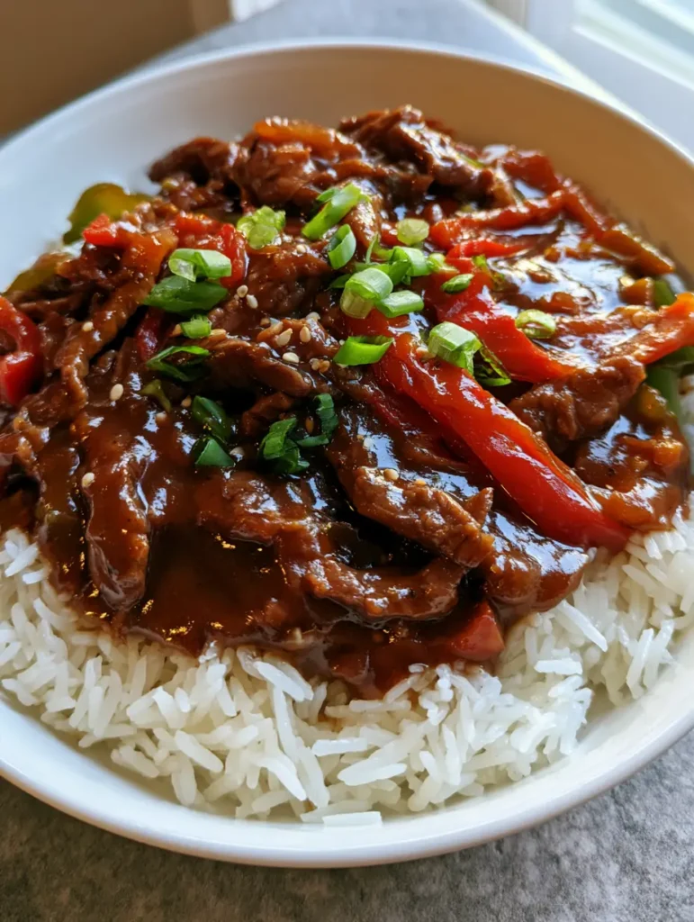 Close-up of tender simmered beef strips in a thick glossy brown gravy for Slow Cooker Pepper Steak.