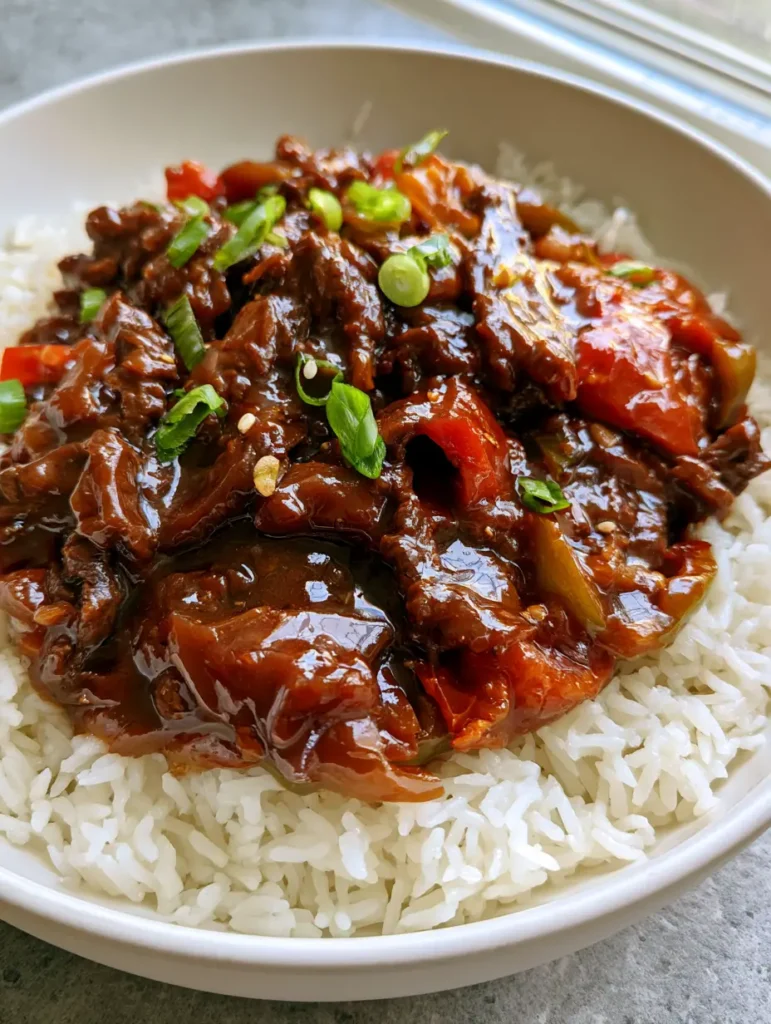 Slow Cooker Pepper Steak: The Ultimate Melt-in-Your-Mouth Recipe 1 A handheld photo of Slow Cooker Pepper Steak garnished with fresh green onions and sesame seeds in a white ceramic bowl.