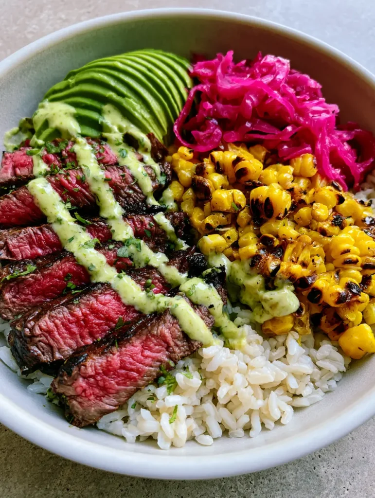 Close up of a Steak and Avocado Bowl showing juicy medium-rare steak slices and charred roasted corn kernels.